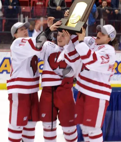 The Wisconsin captains hold the trophy up high. / Matt Rennell